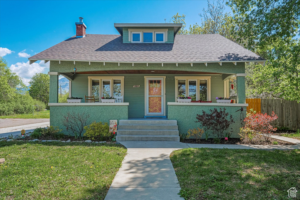 View of front facade featuring a porch, a chimney, a front yard, fence, and a shingled roof