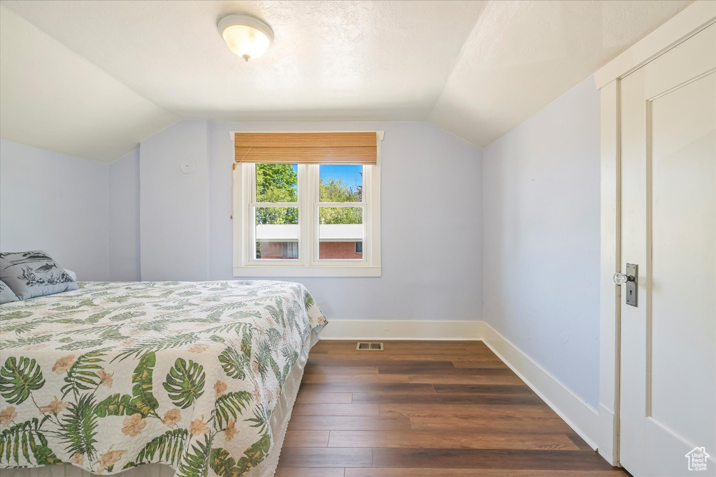 Bedroom featuring baseboards, vaulted ceiling, dark wood-style floors, and visible vents