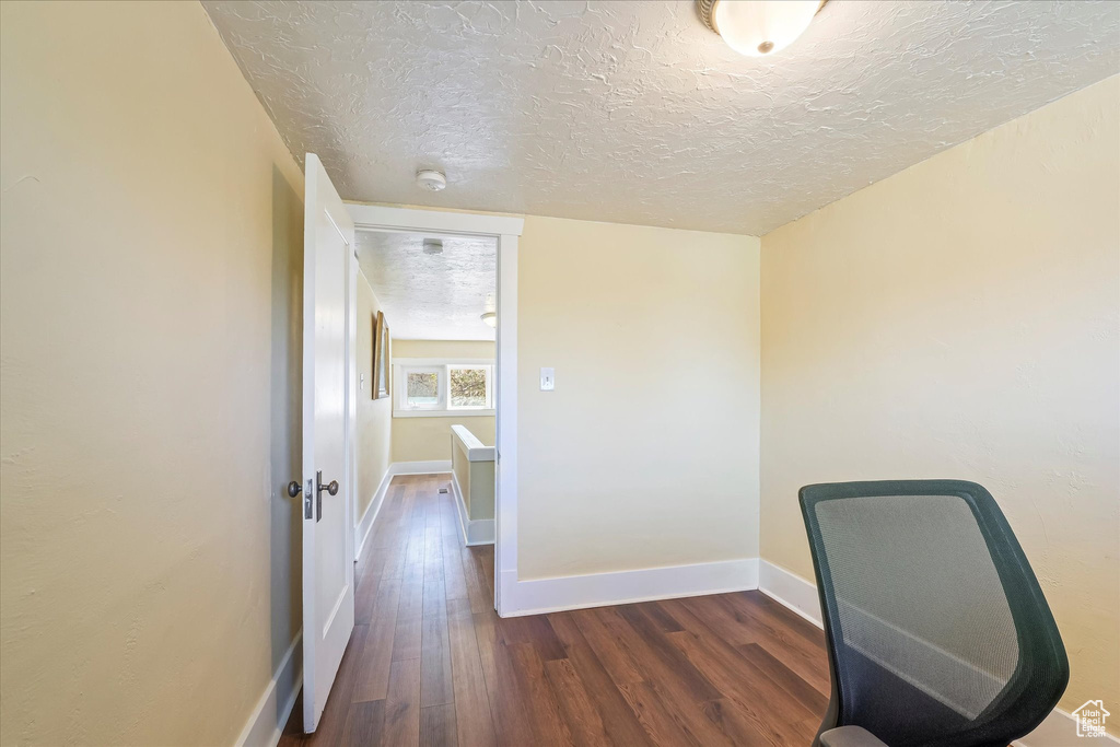 Unfurnished office featuring dark wood-style flooring, a textured ceiling, and baseboards