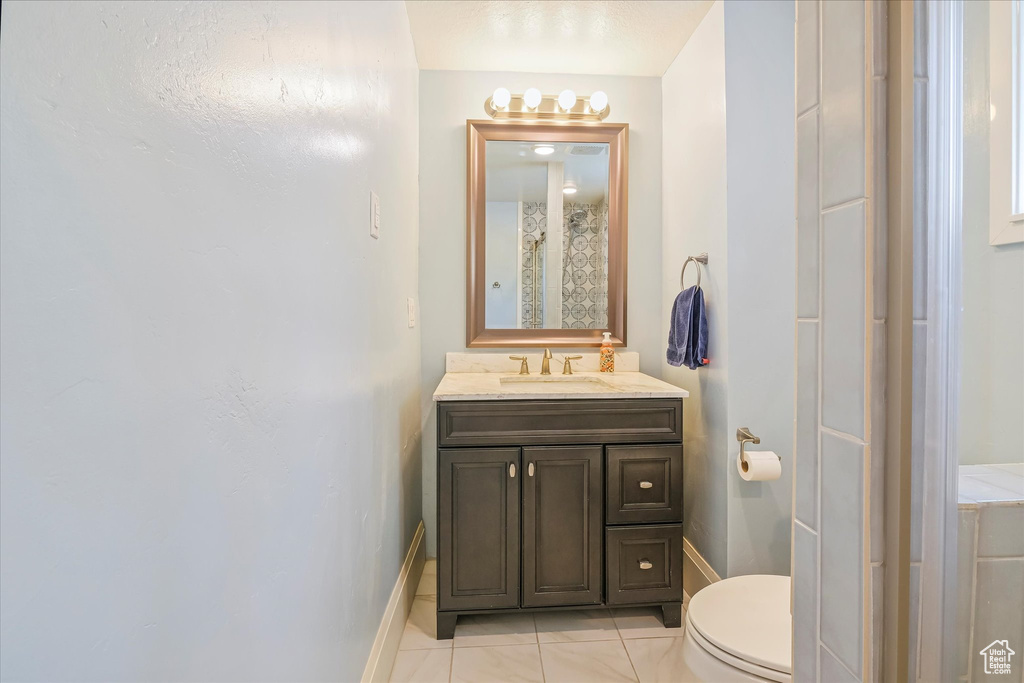 Bathroom with toilet, tile patterned floors, baseboards, and vanity