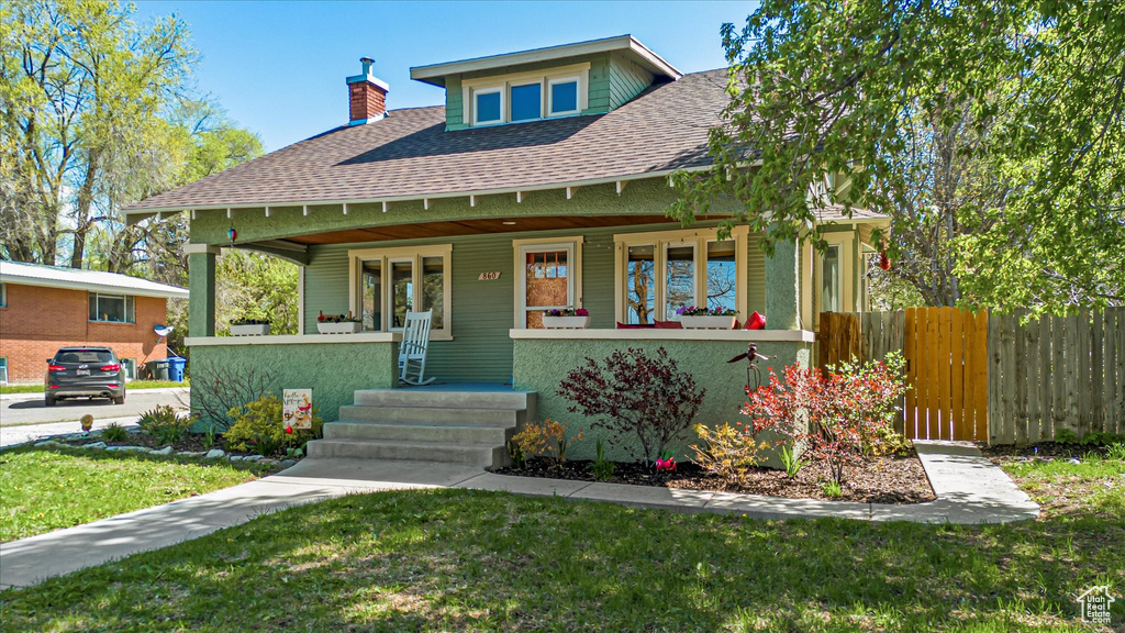 View of front of property featuring a front lawn, fence, a chimney, a shingled roof, and a porch