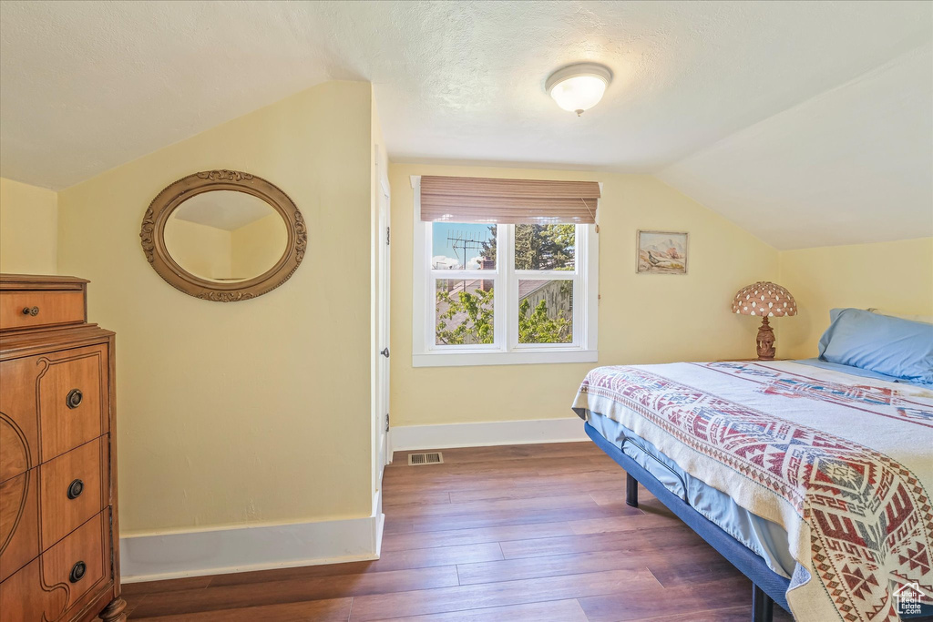 Bedroom featuring dark wood-style flooring, baseboards, visible vents, and lofted ceiling