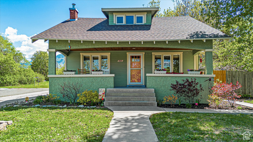 View of front of house with roof with shingles, fence, covered porch, and a chimney