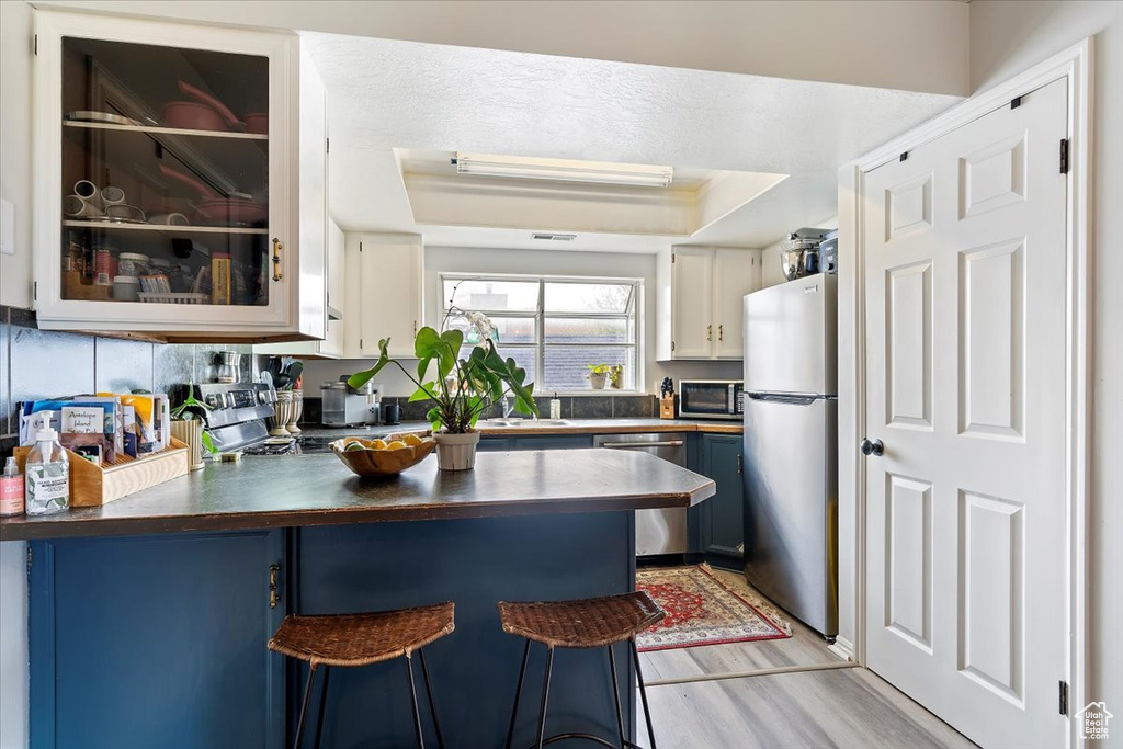 Kitchen featuring a peninsula, dark countertops, stainless steel appliances, light wood finished floors, and blue cabinetry
