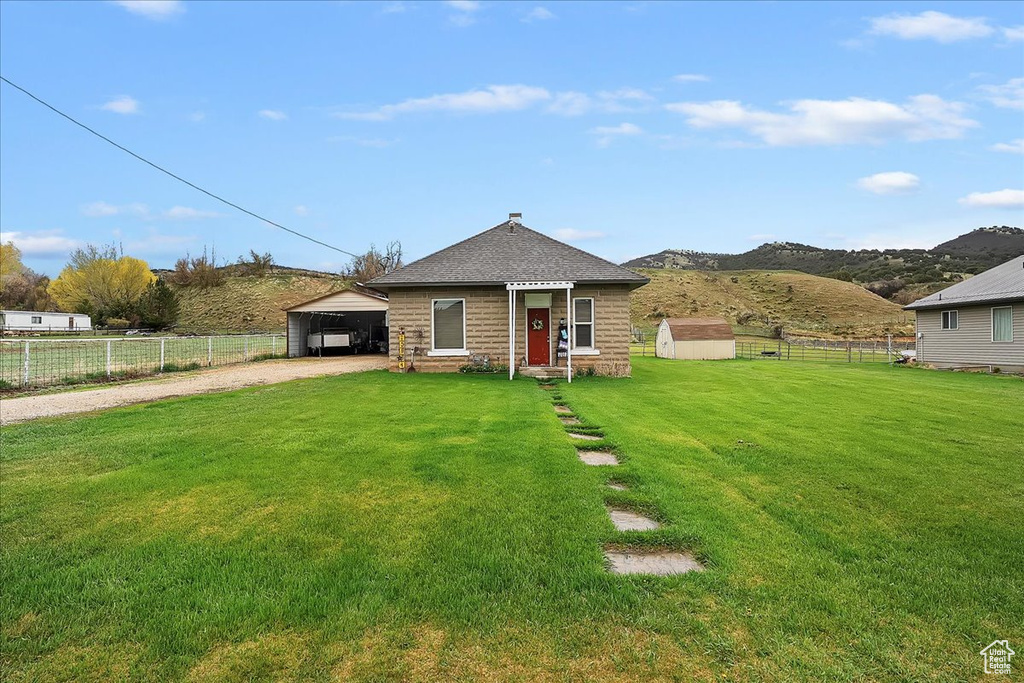 View of front facade featuring a front lawn, fence, dirt driveway, an outbuilding, and a carport