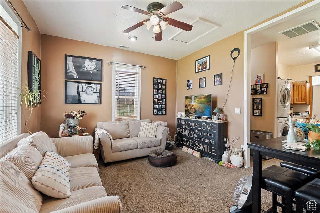 Carpeted living area with stacked washer and dryer, ceiling fan, visible vents, and attic access