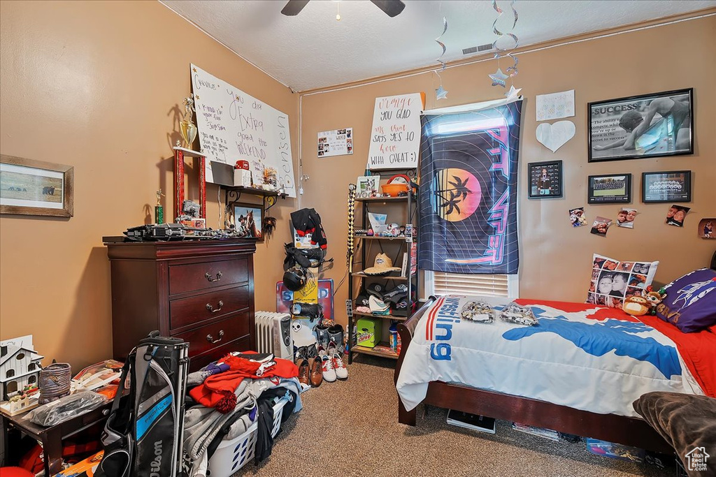 Carpeted bedroom with ceiling fan, visible vents, and radiator