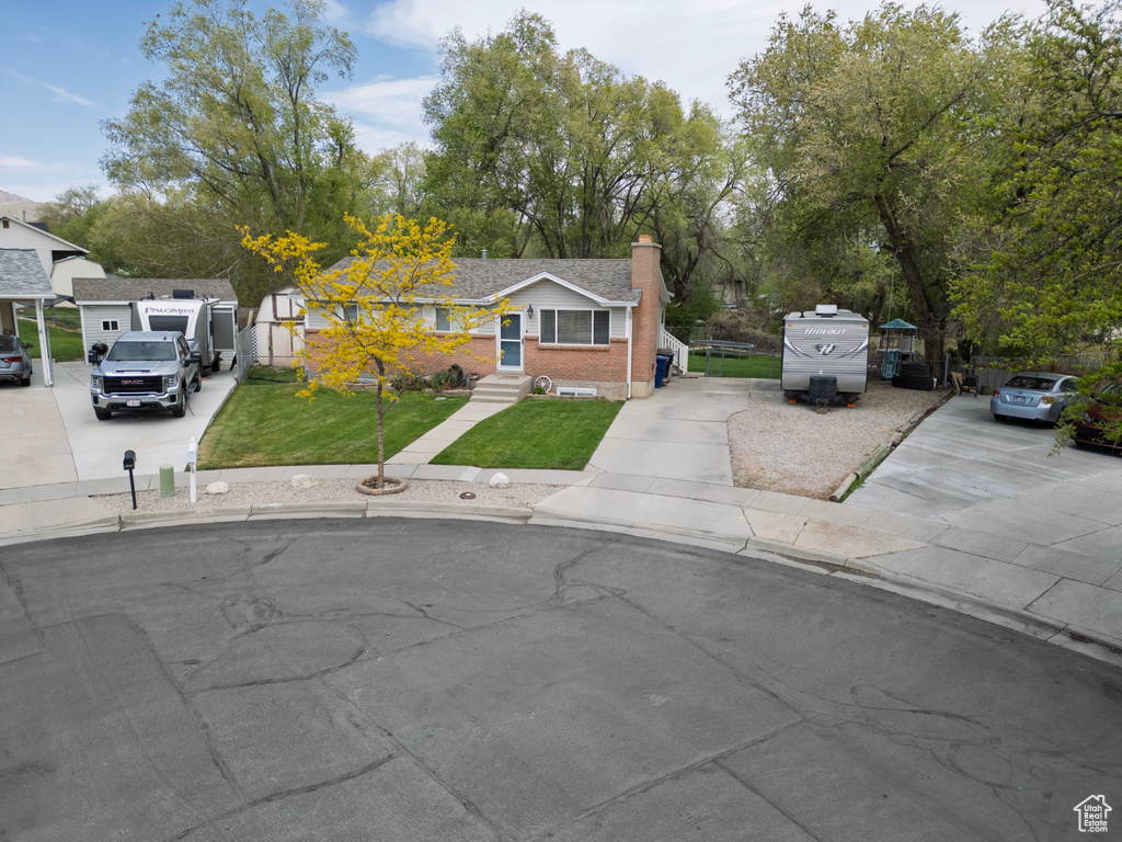 Bungalow-style house with concrete driveway, brick siding, a chimney, and a front yard