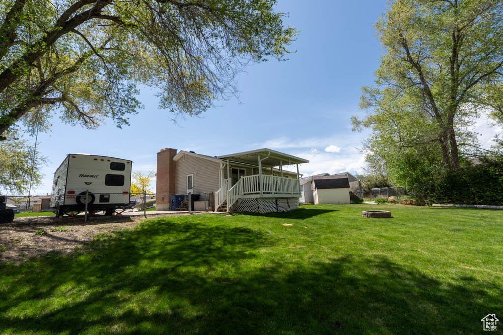 Rear view of property with fence, an outdoor fire pit, a shed, an outbuilding, and a lawn