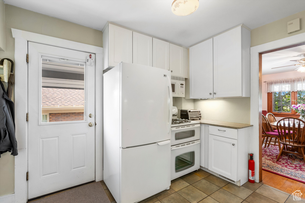Kitchen with white appliances, light countertops, white cabinets, a ceiling fan, and light tile patterned floors