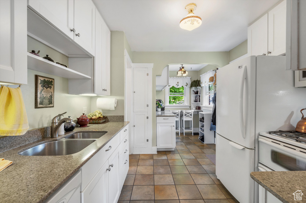 Kitchen featuring open shelves, light stone countertops, arched walkways, white cabinets, and a sink