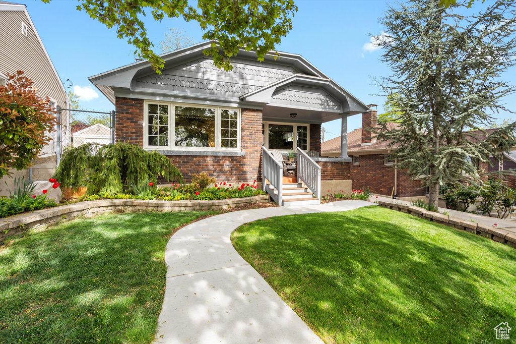 Bungalow-style house with brick siding, fence, covered porch, and a front yard