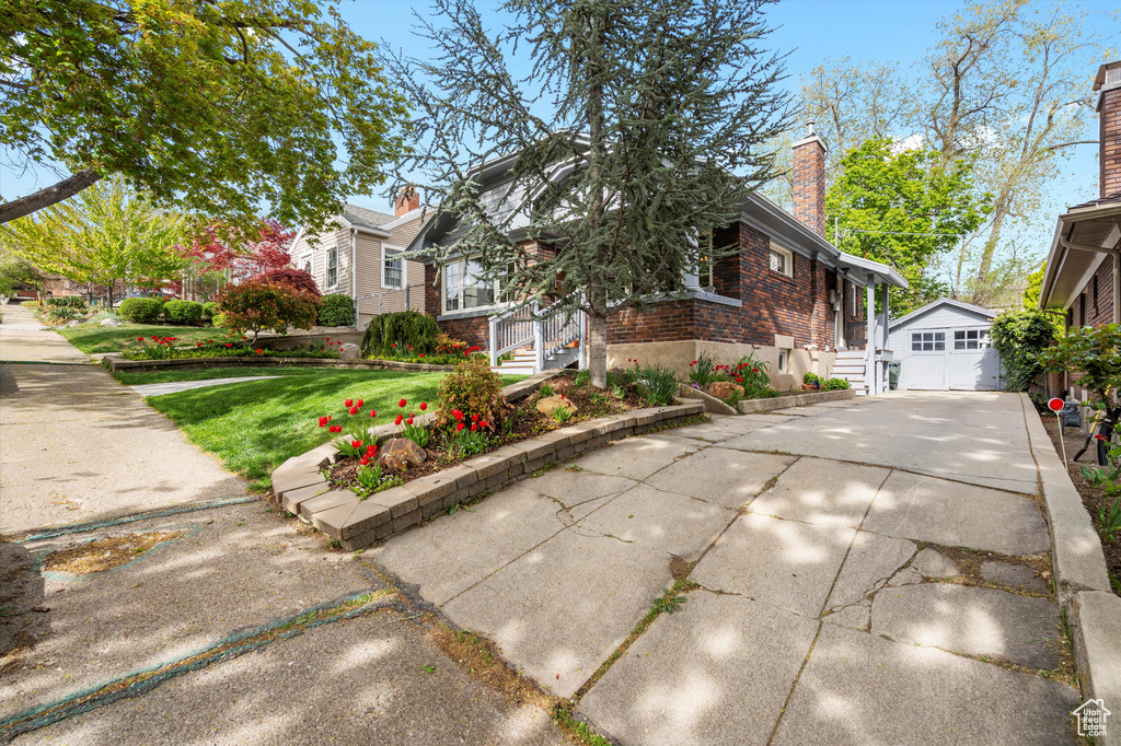 View of front of home featuring a front yard, a chimney, brick siding, concrete driveway, and an outbuilding