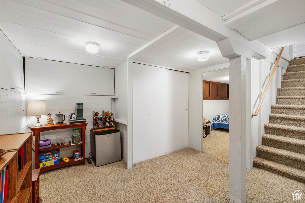 Finished below grade area with fridge, light colored carpet, and stairway