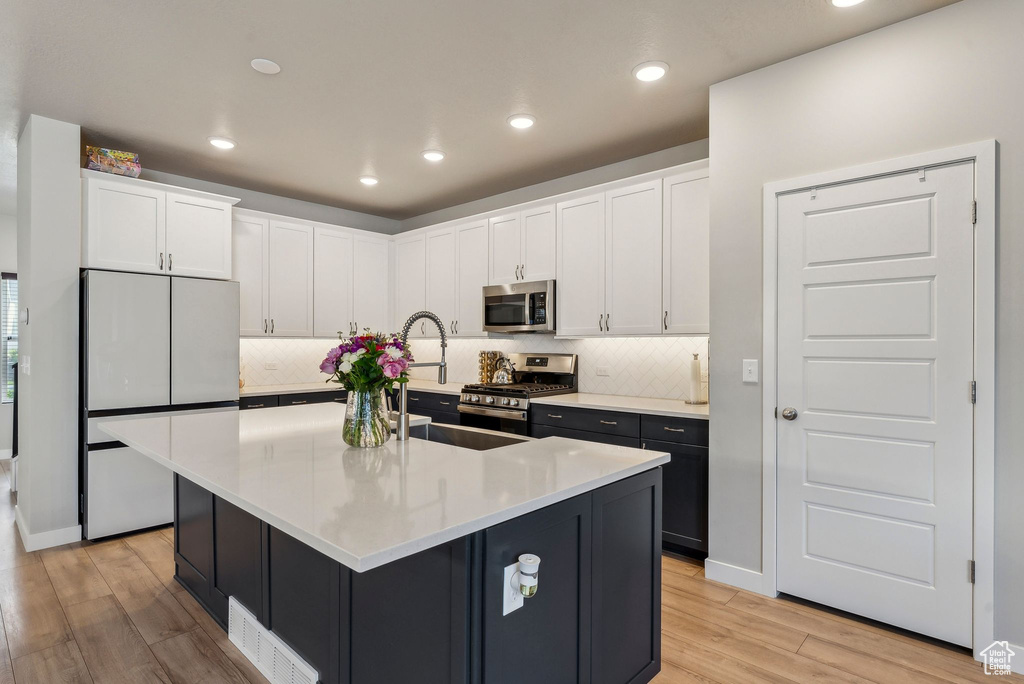 Kitchen with light wood-style floors, backsplash, white cabinets, and stainless steel appliances