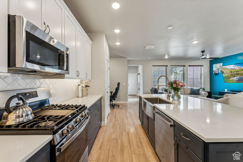 Kitchen featuring white cabinets, open floor plan, appliances with stainless steel finishes, and a sink