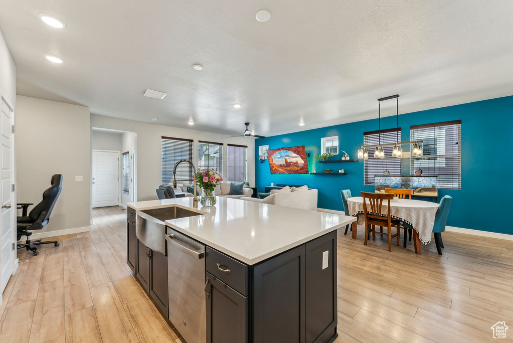 Kitchen featuring a kitchen island with sink, stainless steel dishwasher, a sink, light countertops, and light wood-style floors