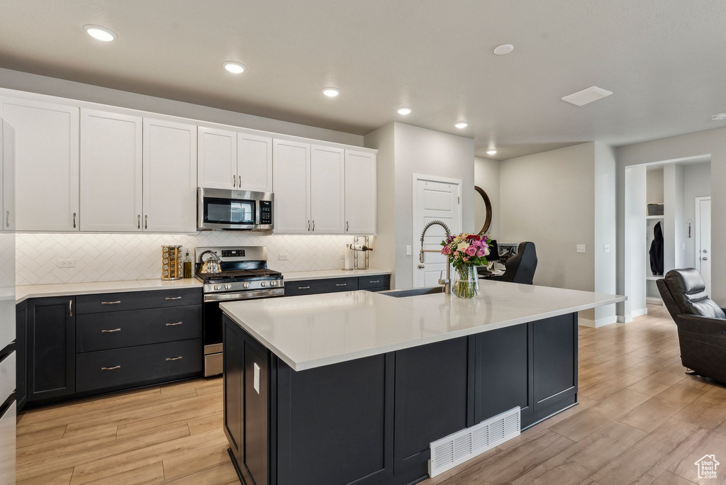 Kitchen with visible vents, appliances with stainless steel finishes, a sink, white cabinets, and light wood finished floors