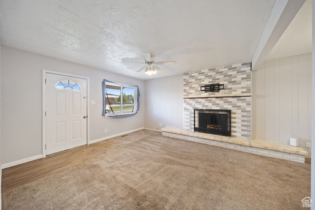 Unfurnished living room with ceiling fan, a brick fireplace, a textured ceiling, carpet, and baseboards