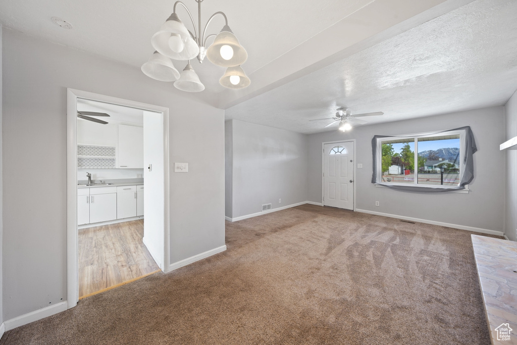 Empty room with light carpet, a sink, ceiling fan with notable chandelier, baseboards, and visible vents