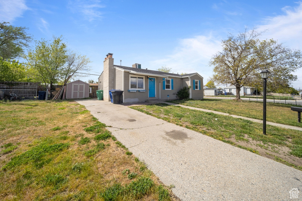 View of front of house with fence, a shed, an outbuilding, a chimney, and concrete driveway