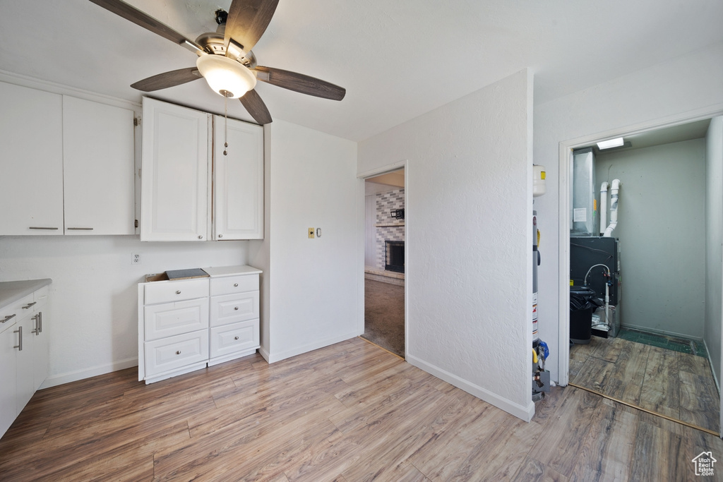 Interior space with light wood-type flooring, a brick fireplace, white cabinetry, and ceiling fan