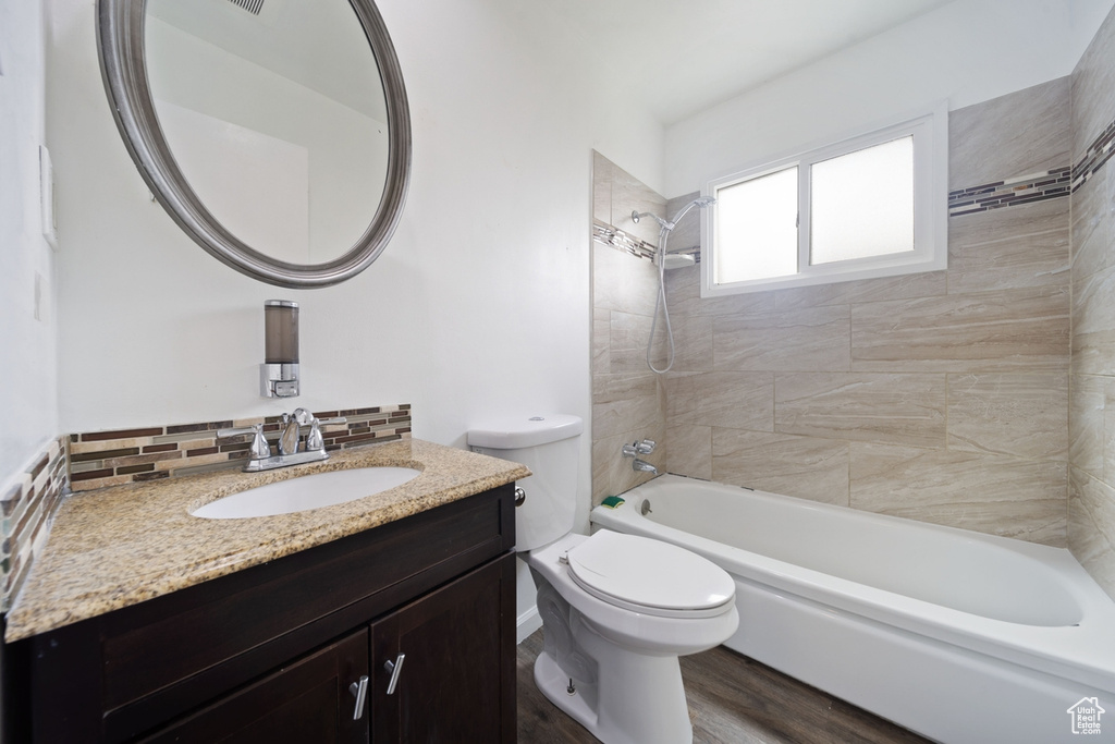 Full bathroom with vanity, toilet, decorative backsplash, bathing tub / shower combination, and wood finished floors