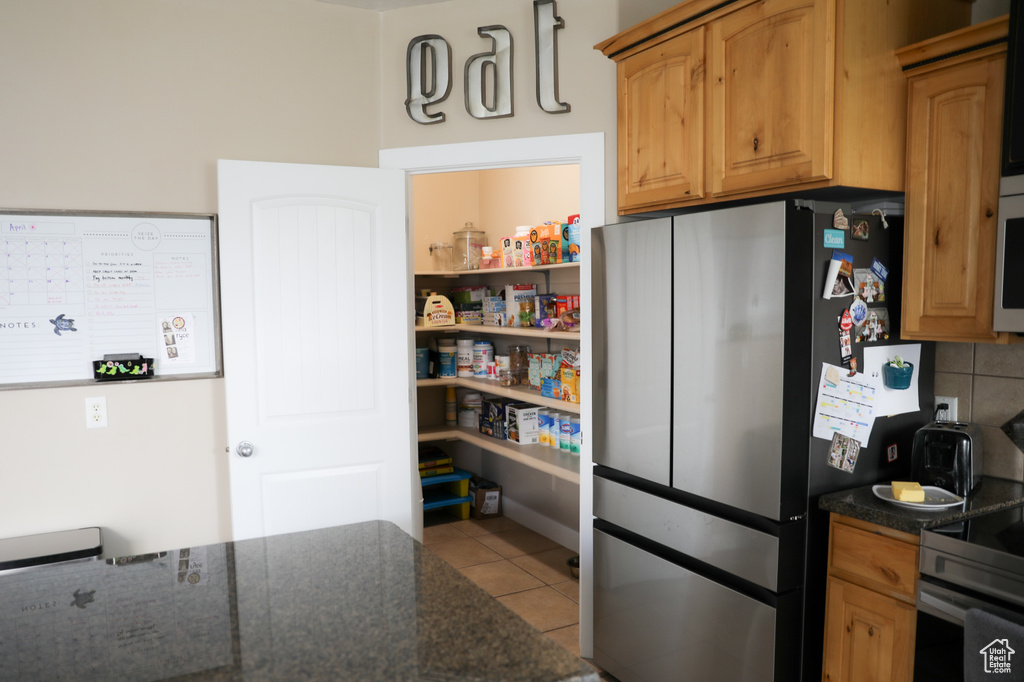 Kitchen featuring tile patterned floors, freestanding refrigerator, dark stone countertops, and electric stove