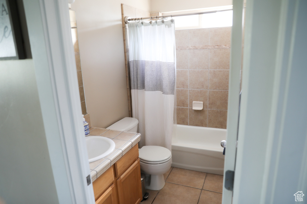 Bathroom featuring vanity, shower / bathtub combination with curtain, tile patterned floors, and toilet