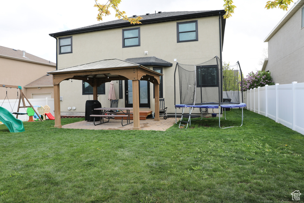 Rear view of property featuring a trampoline, a patio area, a gazebo, a yard, and stucco siding