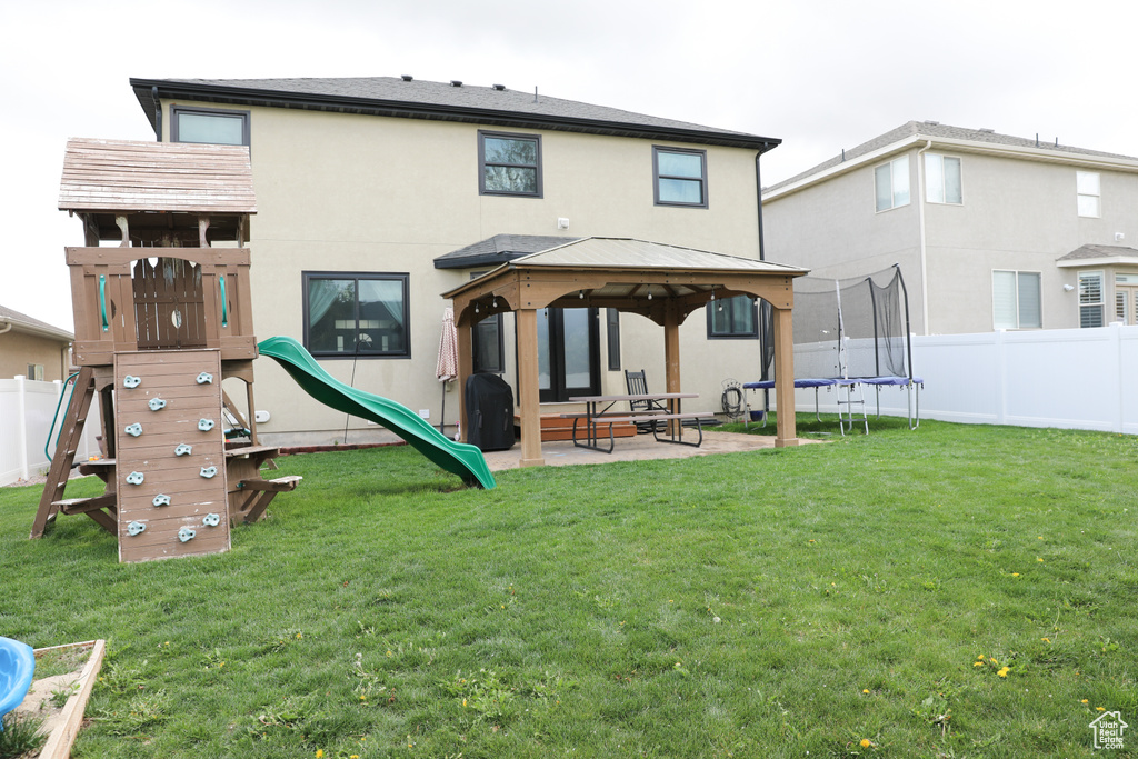 Back of house with a fenced backyard, a trampoline, a gazebo, and stucco siding