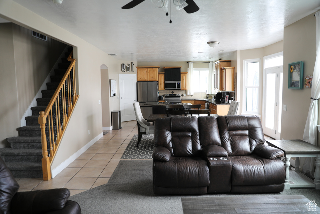 Living room with arched walkways, a ceiling fan, baseboards, light tile patterned floors, and stairway