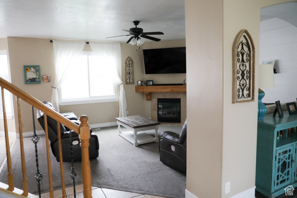 Carpeted living room featuring a ceiling fan, arched walkways, a tile fireplace, stairway, and baseboards