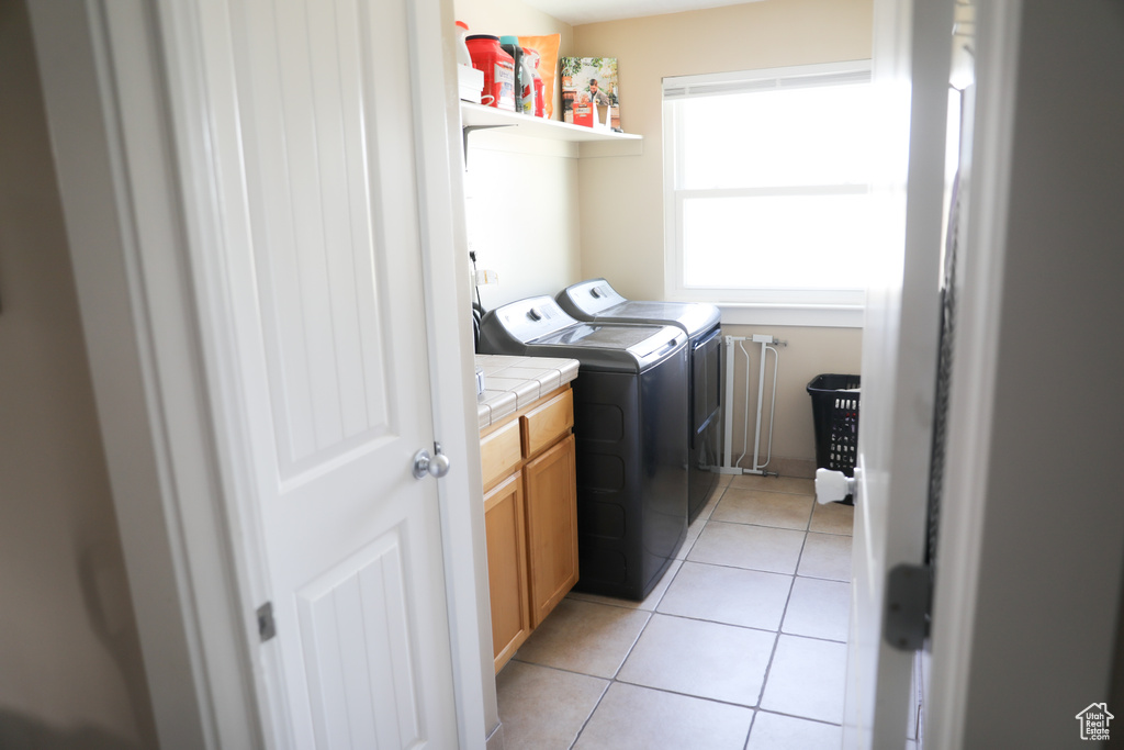 Clothes washing area with separate washer and dryer, cabinet space, and light tile patterned flooring