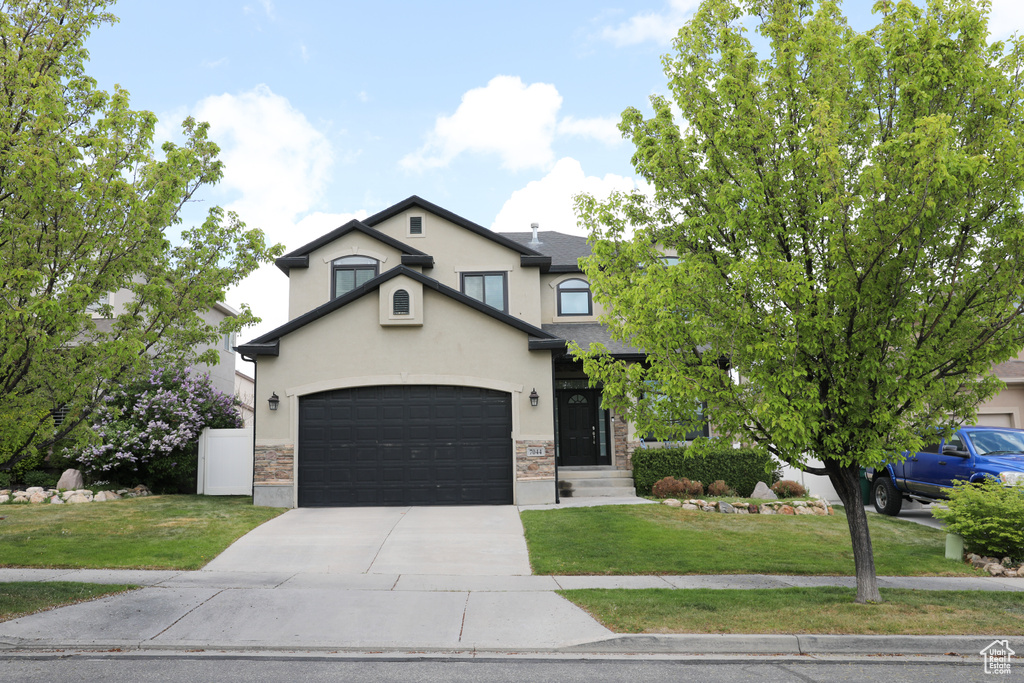 View of front of property featuring stucco siding, driveway, stone siding, and a front yard