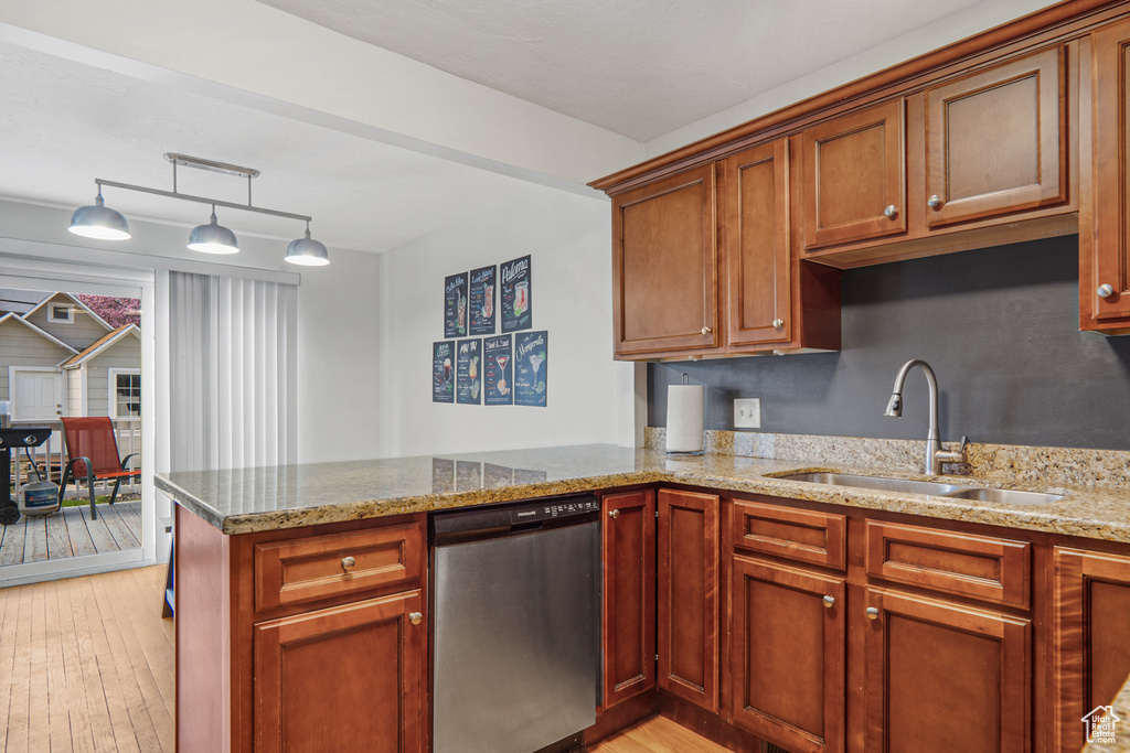 Kitchen featuring dishwasher, a sink, light stone counters, light wood finished floors, and a peninsula
