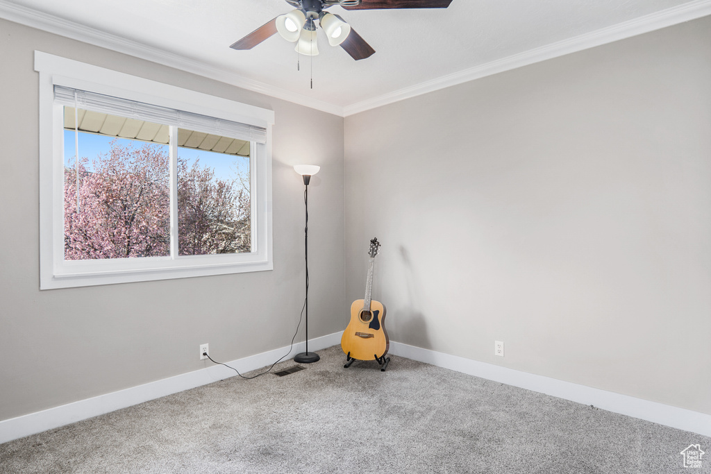 Carpeted empty room featuring crown molding, a ceiling fan, baseboards, and visible vents