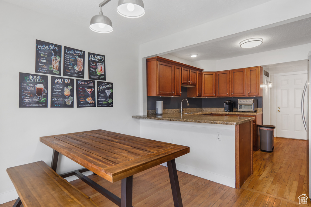 Kitchen featuring a sink, a peninsula, dark stone countertops, stainless steel fridge, and light wood-style flooring