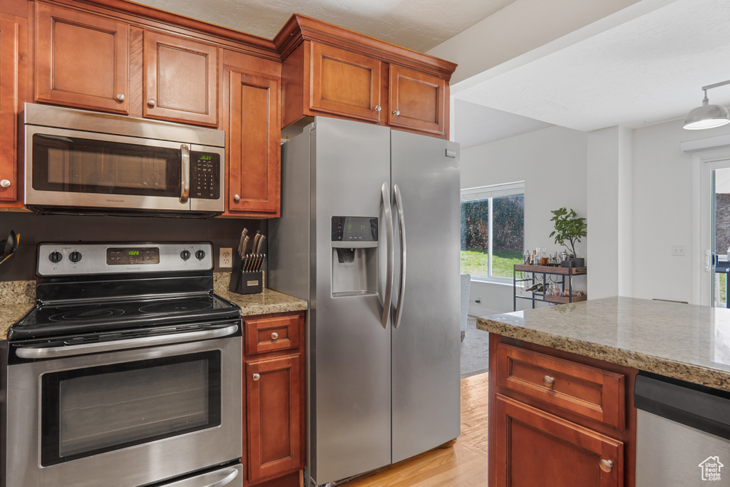 Kitchen with brown cabinetry, light wood finished floors, light stone countertops, and stainless steel appliances