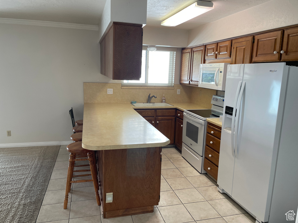 Kitchen featuring a sink, light countertops, a peninsula, ornamental molding, and white appliances