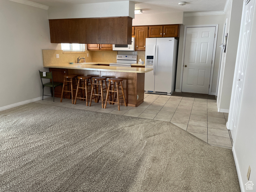 Kitchen featuring ornamental molding, a peninsula, light carpet, and white appliances