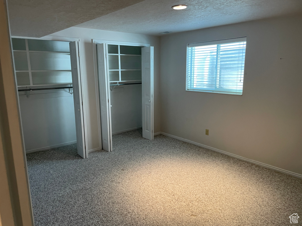 Unfurnished bedroom with baseboards, a textured ceiling, two closets, and light carpet