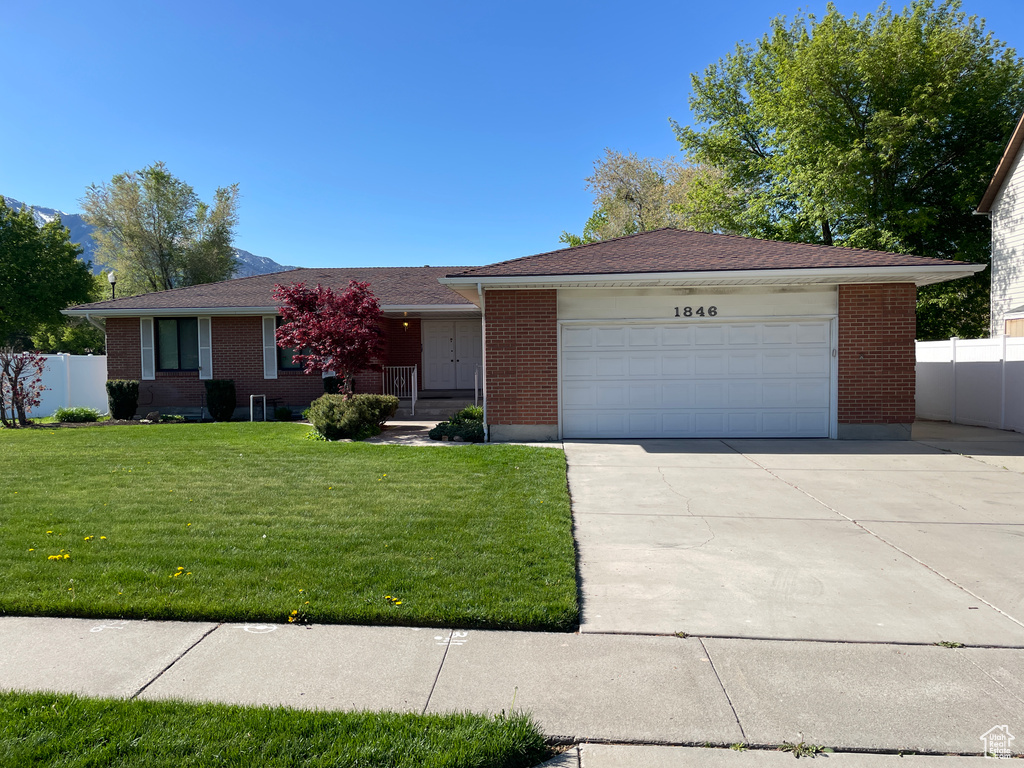 Ranch-style house featuring fence, an attached garage, a front lawn, brick siding, and driveway