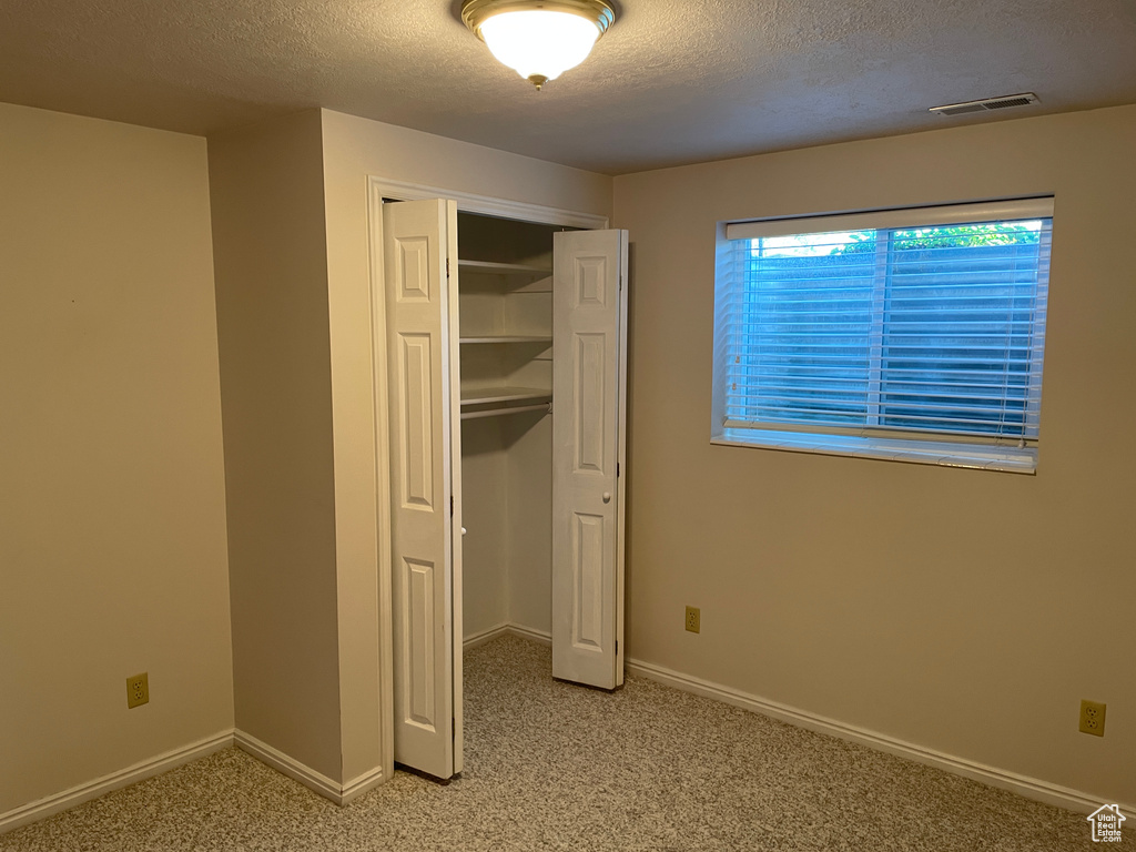 Unfurnished bedroom featuring light colored carpet, a textured ceiling, visible vents, and a closet