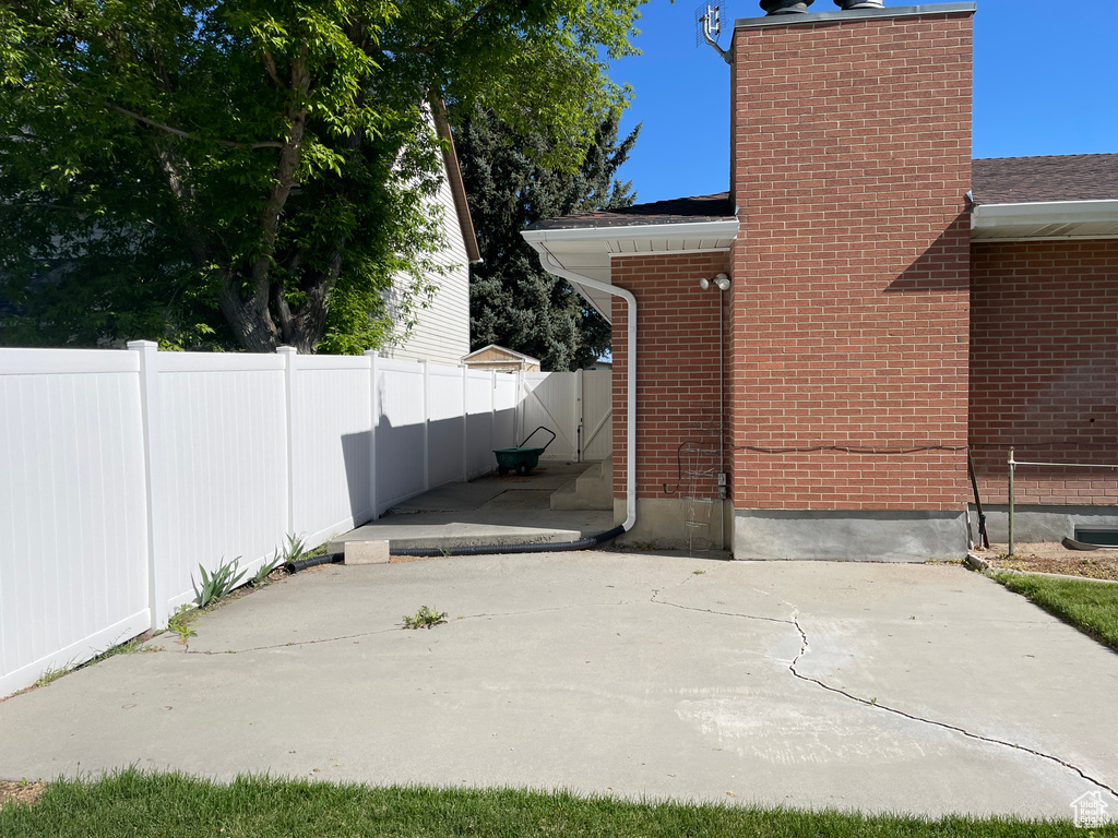 View of side of home featuring fence, a chimney, a patio area, and brick siding