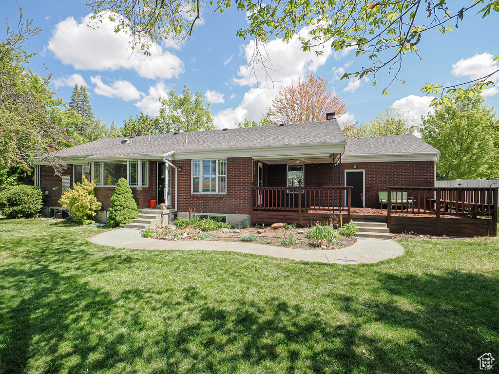 View of front facade featuring brick siding, a wooden deck, a chimney, and a front lawn