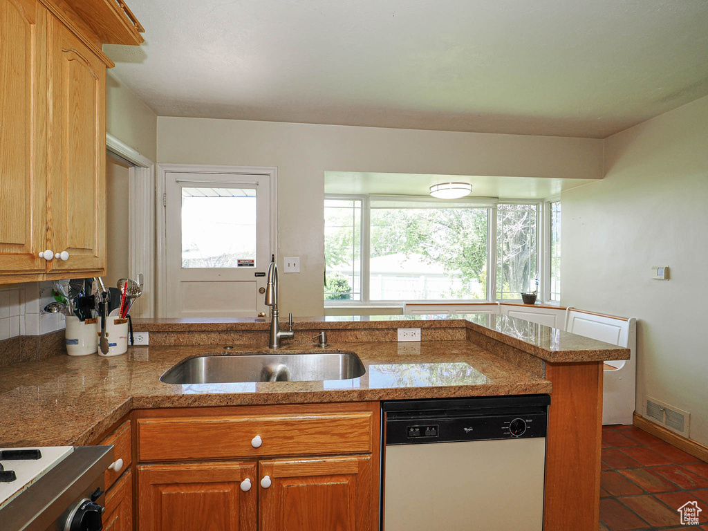 Kitchen with white dishwasher, a sink, range, brown cabinetry, and visible vents
