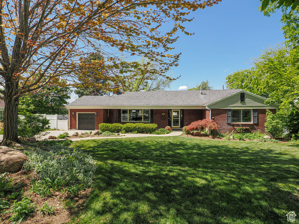 Ranch-style house featuring brick siding, an attached garage, fence, and a front yard
