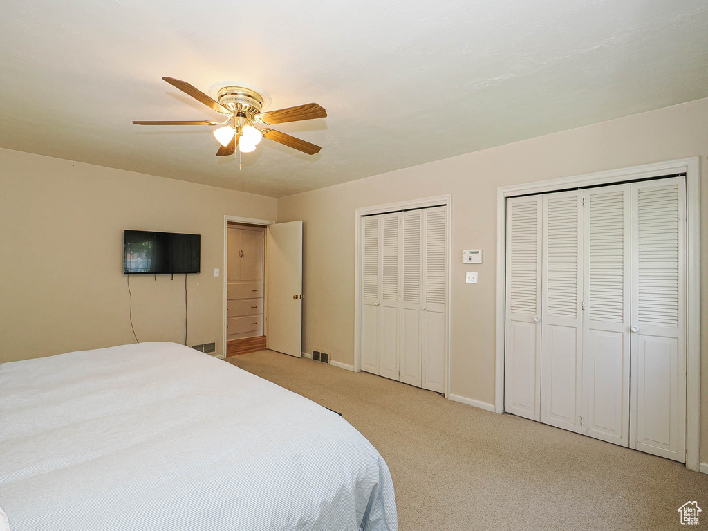 Bedroom featuring light colored carpet, multiple closets, a ceiling fan, baseboards, and visible vents