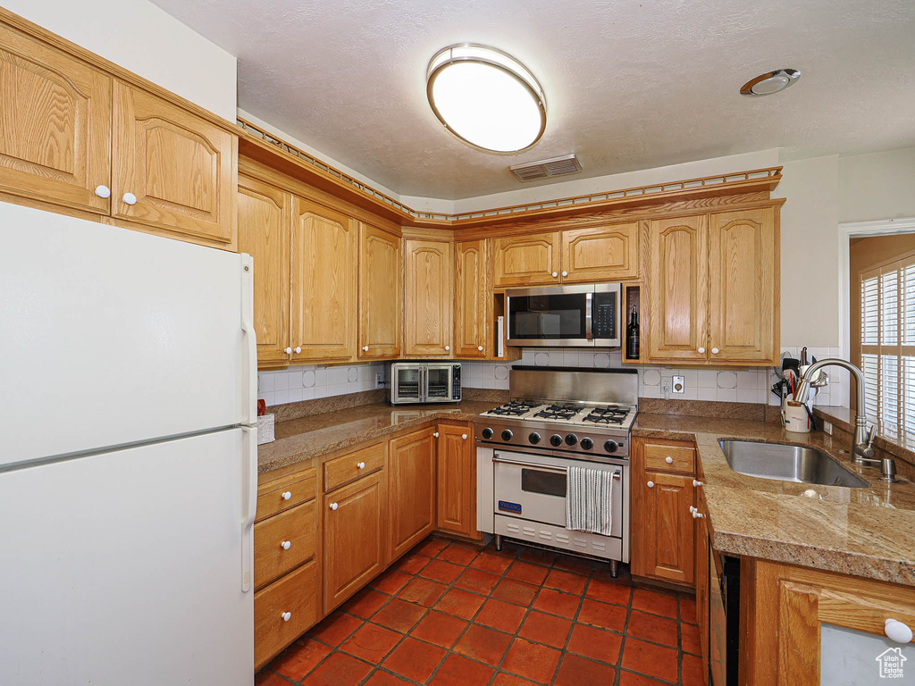 Kitchen with visible vents, decorative backsplash, dark tile patterned flooring, a sink, and stainless steel appliances